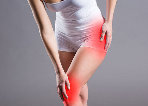 Woman holding hip and knee, both lit up in red, in pain