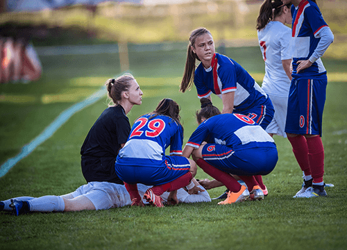Soccer players on the field gathered around an injured player on the ground.