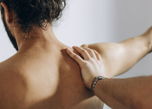 Hand examining the back of a patient's bare shoulder